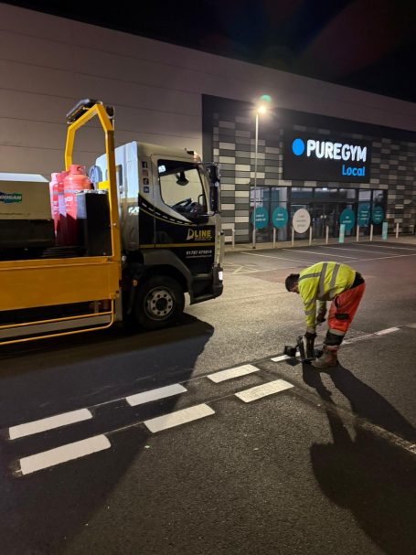 A worker in high-visibility apparel is repainting road markings at night.