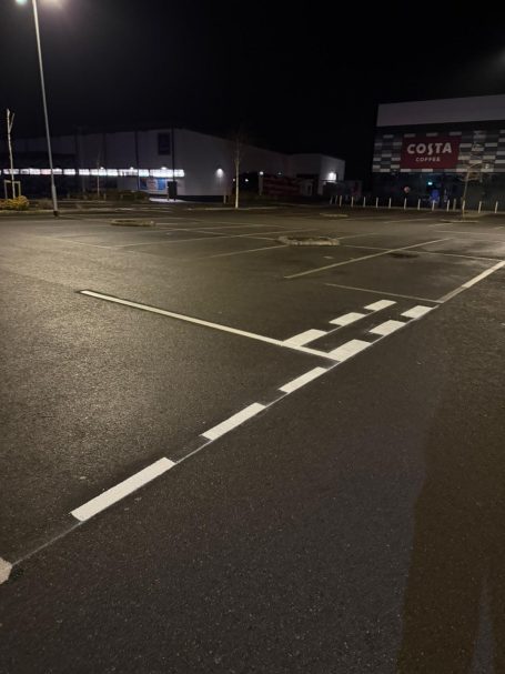 Empty car park at night with faint lighting and painted white lines on the asphalt.