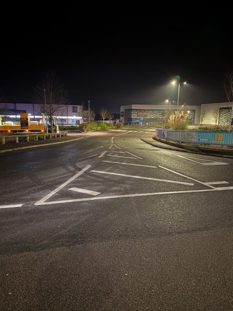 Nighttime scene of an empty road with marked lanes and buildings in the background.