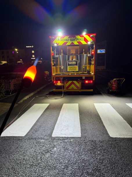 Emergency vehicle parked at a crosswalk, illuminated by bright lights at night.